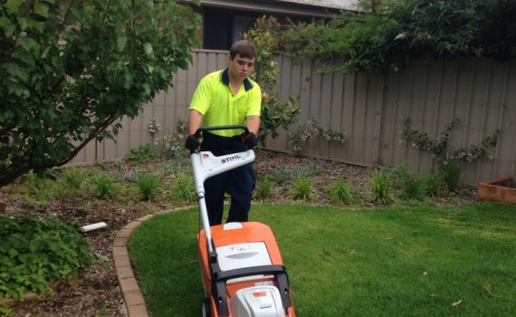 a young man in high vis shirt mowing a back lawn