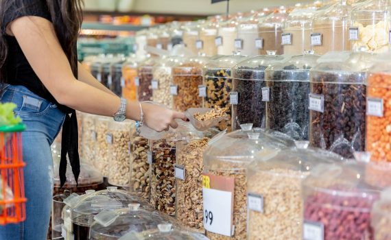 A woman's arm and torso is shown, she is scooping nutes from a range of bulk jars in a food store