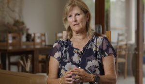 A woman with light brown hair is speaking, as if being interviewed.