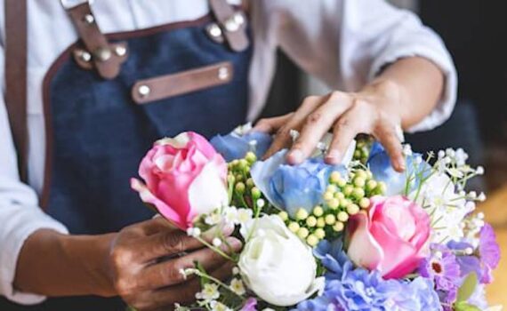 close up of a florist arranging a bunch of pink, yellow and blue rose like flowers