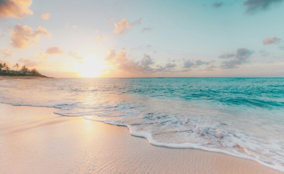 Foamy shoreline on a white sandy beach. Sun setting into low clouds