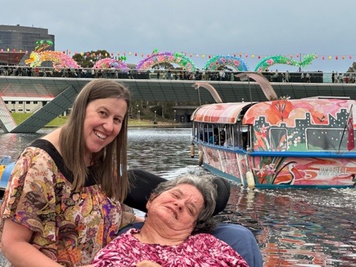 A vibrant scene on the River Torrens. Two women pose for the camera, behind them a Chinese dragon lantern stretches the length of the footbridge, the Popeye riverboat is also decorated for the moon lantern festival.